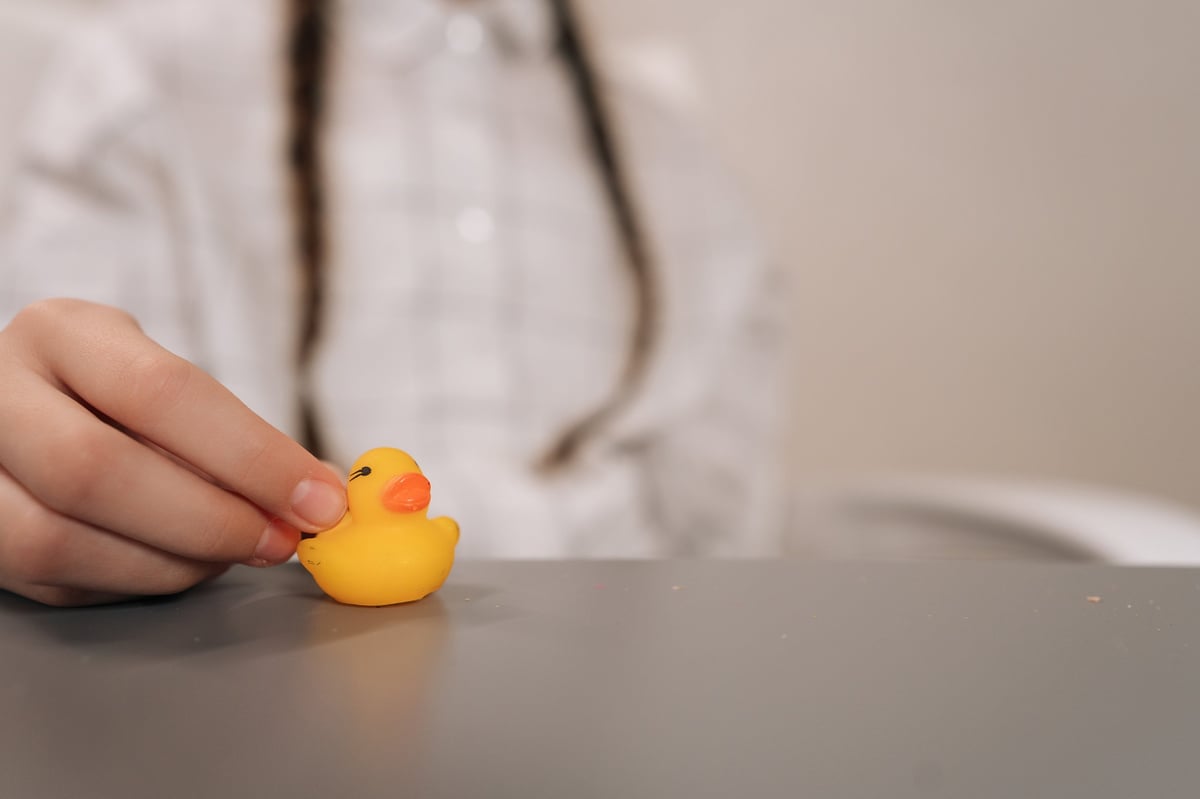 Child with braids holding a small yellow squishy toy, exploring its soft texture