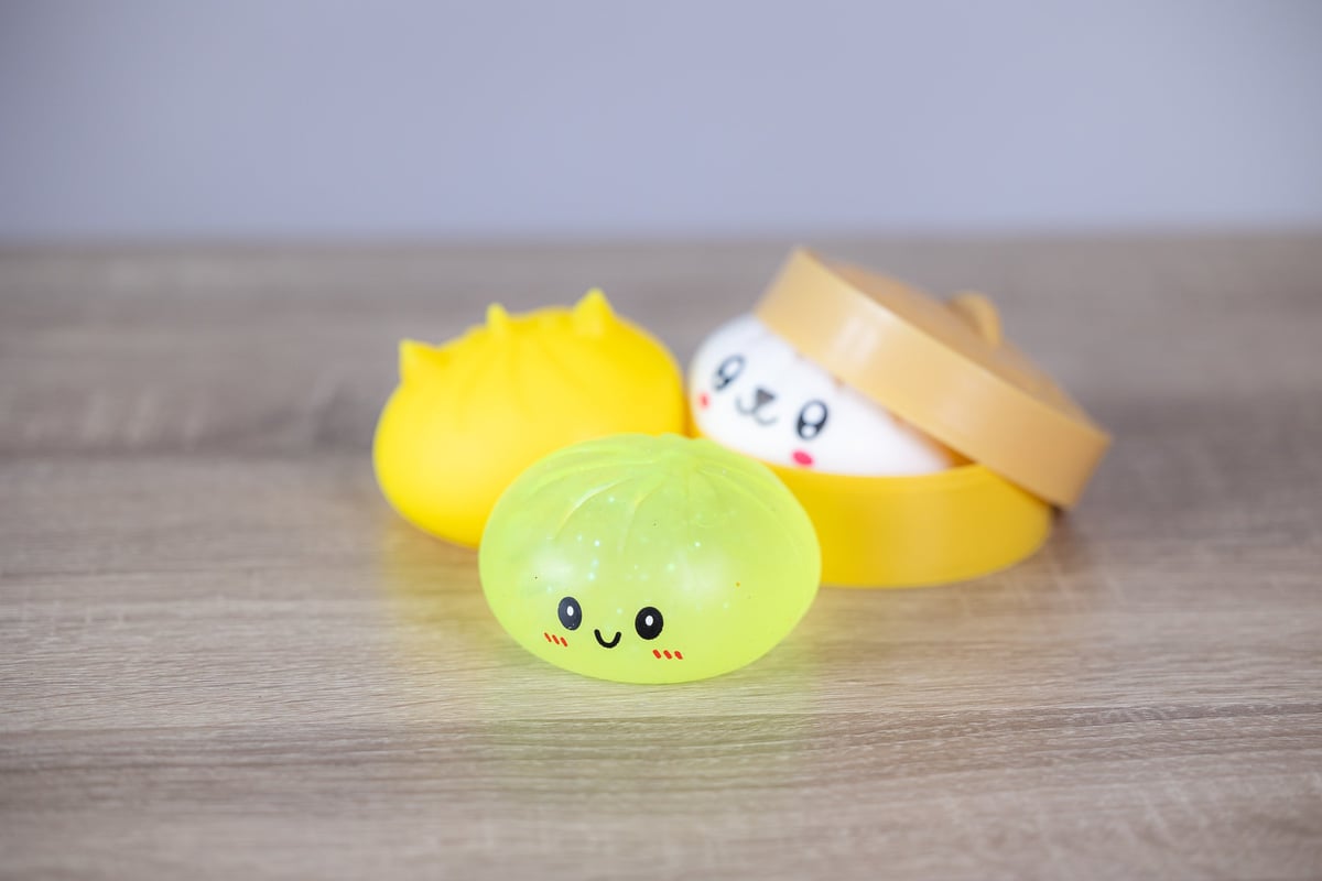 Close-up of a small round squishy toy with a smiling face and blushed cheeks on a light wood surface